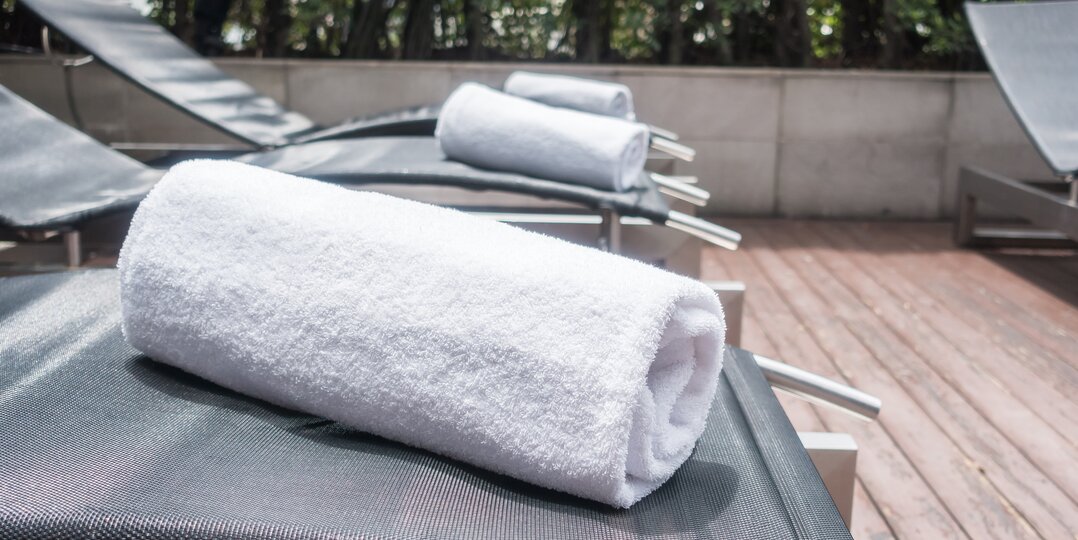 Dussmann's laundry service for wellness areas, providing soft, clean and hygienic linen tailored to the needs of spas, wellness centers and hotels, while adhering to strict hygiene and quality protocols. | © <a href="https://www.freepik.com/free-photo/white-towels-deck-chairs_952848.htm">Image by mrsiraphol on Freepik</a>